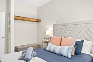Un lit bien fait, avec une couvre-lit à motifs, une tête de lit capitonnée et plusieurs coussins.