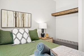 A neatly made bed with green bedding, a pillow with a geometric pattern, and a rolled towel on the side. - The Rooftop Haven of Downtown (1012 Franklin St) (Clarksville)