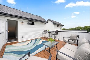 Une terrasse extérieure couverte avec une plateforme en bois, un tapis à rayures et du mobilier d’extérieur comprenant un canapé et des fauteuils.