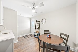 Une cuisine moderne avec des meubles blancs, une table à manger en bois et un ventilateur de plafond.
