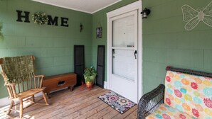 A porch with a wooden bench, a rocking chair, a colorful cushion, a welcome mat, and a wall with the word 'HOME' and a butterfly decoration. - Hometown Clarksville Cottage (1021 Crossland Ave) (Clarksville)
