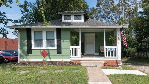 A single-story house with a front porch, a welcome sign, and an American flag. - Hometown Clarksville Cottage (1021 Crossland Ave) (Clarksville)
