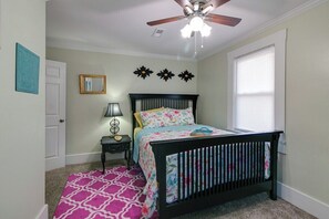 A bedroom with a bed, a ceiling fan, a window with blinds, and a door.