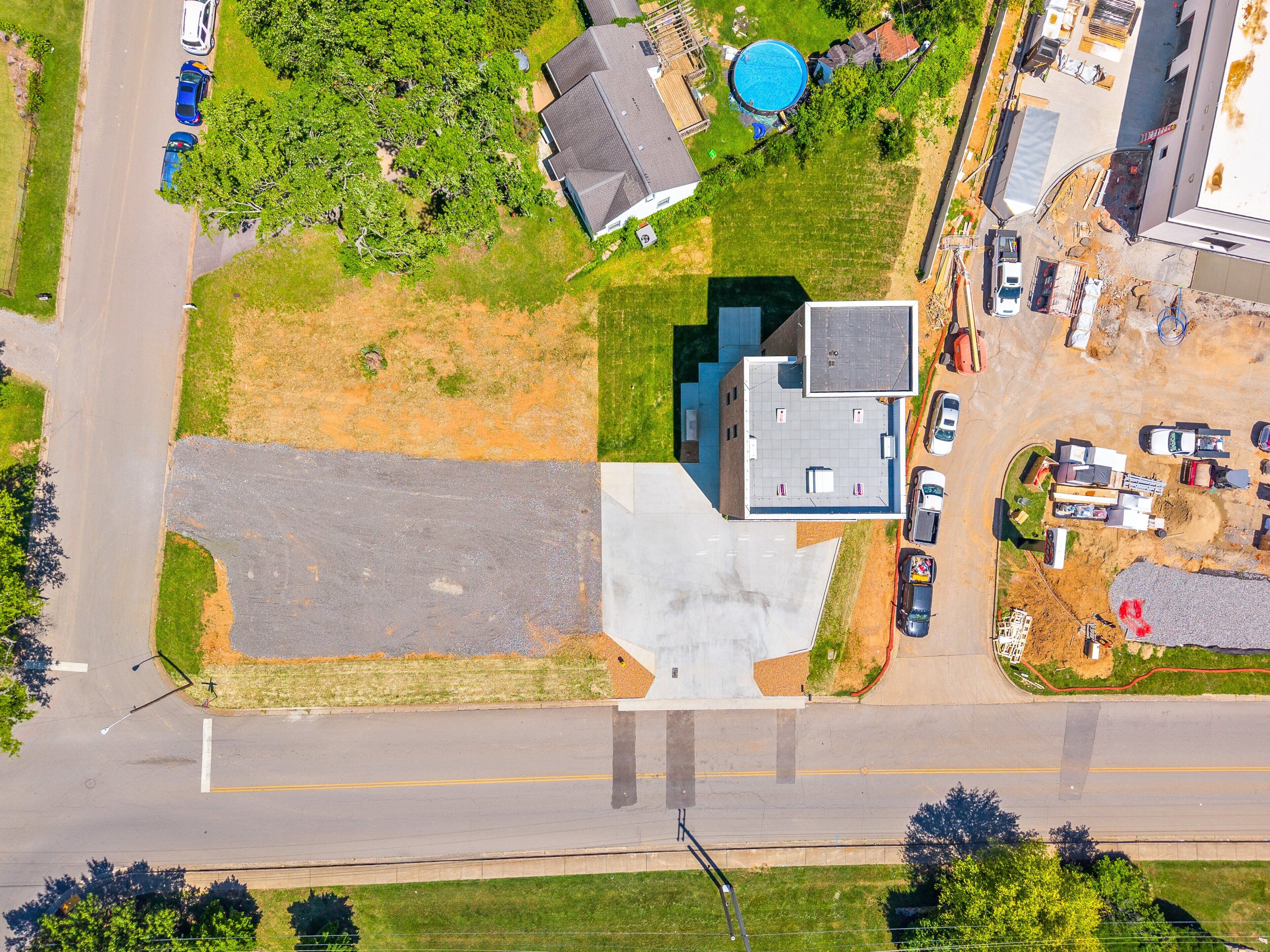 An aerial view of a residential area with a large parking lot, a swimming pool, and a building with a flat roof.