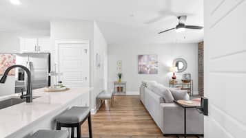 A modern kitchen with a central island, a dining area with a sofa and table, and a ceiling fan.