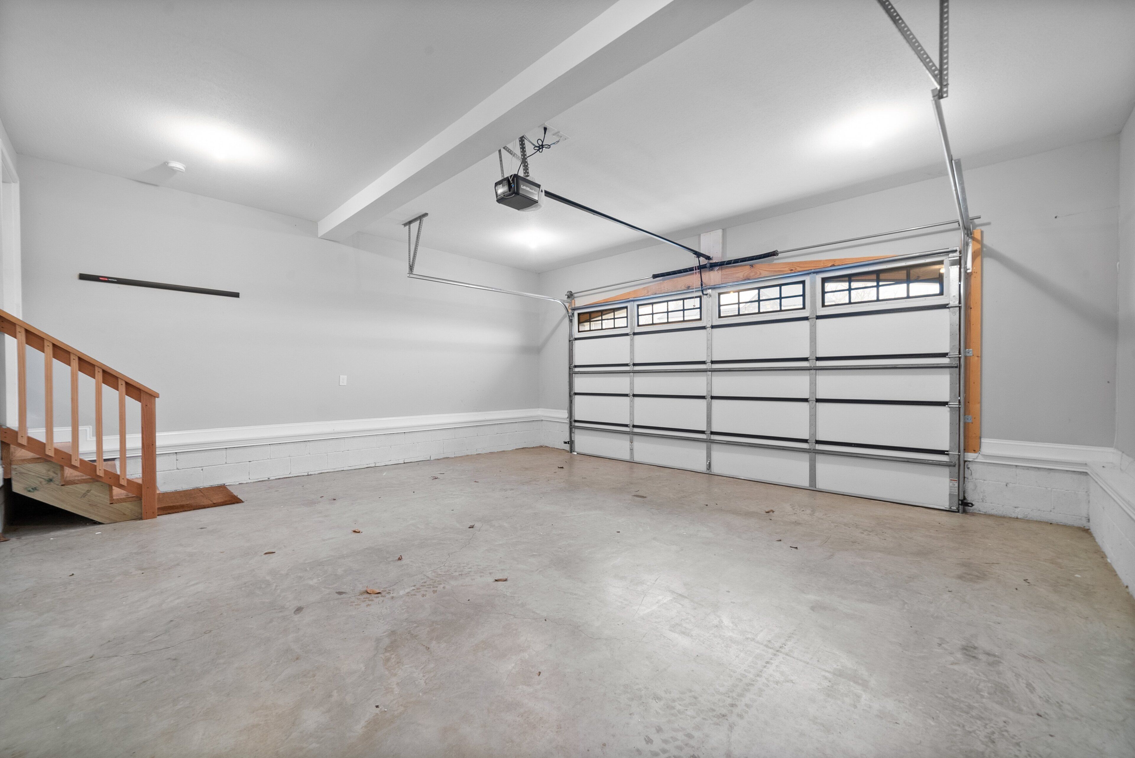 Un garage propre et vide, avec un escalier en bois, une porte de garage en métal et un éclairage au plafond.