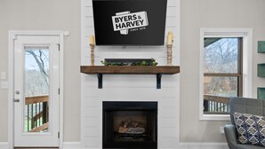 Een woonkamer met een open haard, een wandtelevisie en een deur naar een terras.