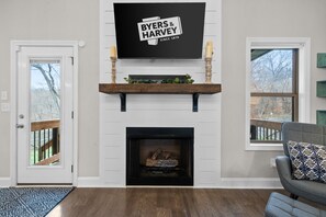 Ein Wohnzimmer mit Kamin, einem an der Wand befestigten Fernseher und einer Tür zu einer Terrasse.