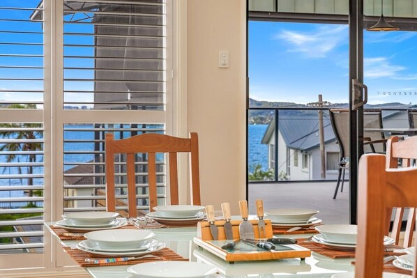Ein Essbereich mit einem Tisch für vier Personen, einem Holzstuhl und Blick auf das Meer durch ein großes Fenster.