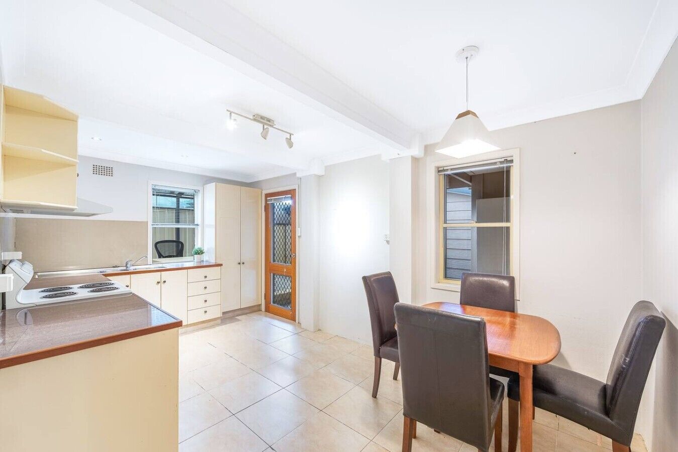 A kitchen with a stove, cabinets, and a dining area with chairs and a table.