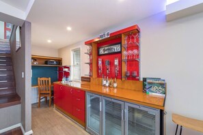 A compact kitchen with a red countertop, a built-in refrigerator, and a bar area with glassware. - Waterfront Games House | Pool & Bay Views (Koolewong)