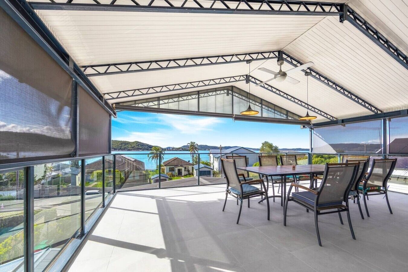 A covered outdoor dining area with a view of the sea and hills.