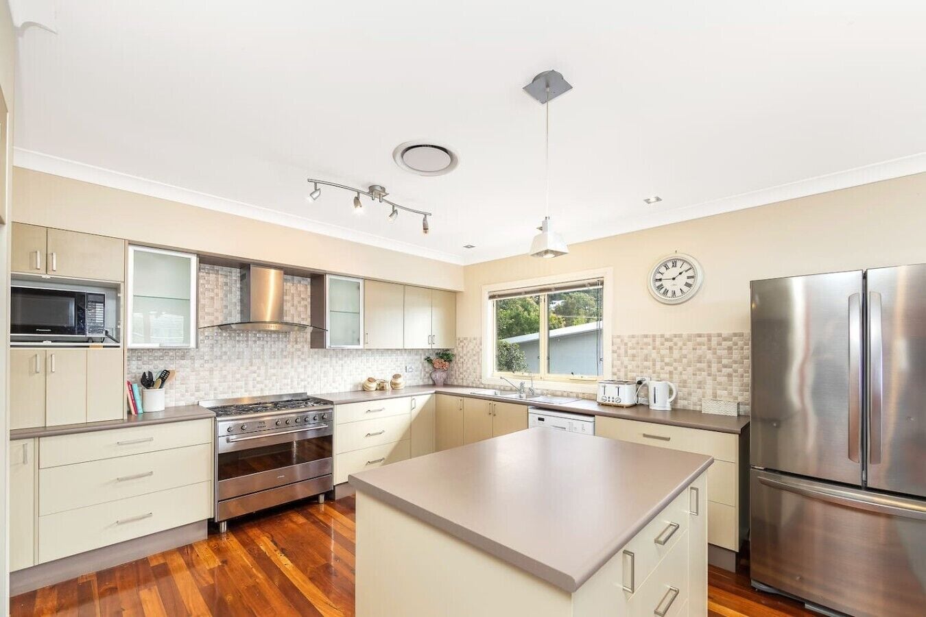 A modern kitchen with a central island, stainless steel appliances, and a large window providing natural light.