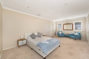 A bedroom with a bed, bedside tables, a blue sofa set, and a large mirror. - Waterfront Games House | Pool & Bay Views (Koolewong)