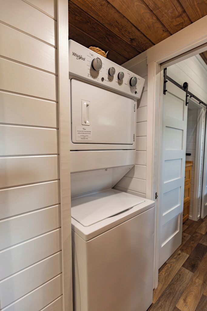 Ein kleiner Waschraum mit einer Whirlpool Waschmaschine und einem Trockner, Holzboden und einer weißen Außenwand.