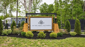 A sign for 'In the Pines Cottages' at Kentucky Lake, surrounded by landscaped garden beds and a wooden fence.