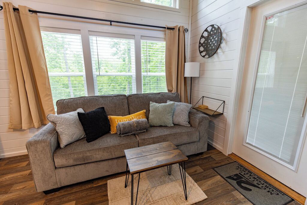 Ein Wohnzimmer mit grauem Sofa, einem Holztisch und einem Fenster mit Vorhängen.