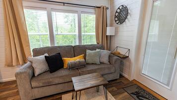 Ein Wohnzimmer mit grauem Sofa, einem Holztisch und einem Fenster mit Vorhängen.
