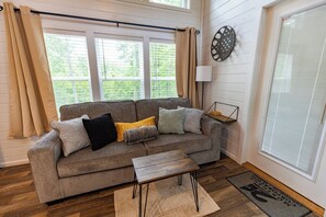 A living room with a grey sofa, a wooden coffee table, and a window with curtains.