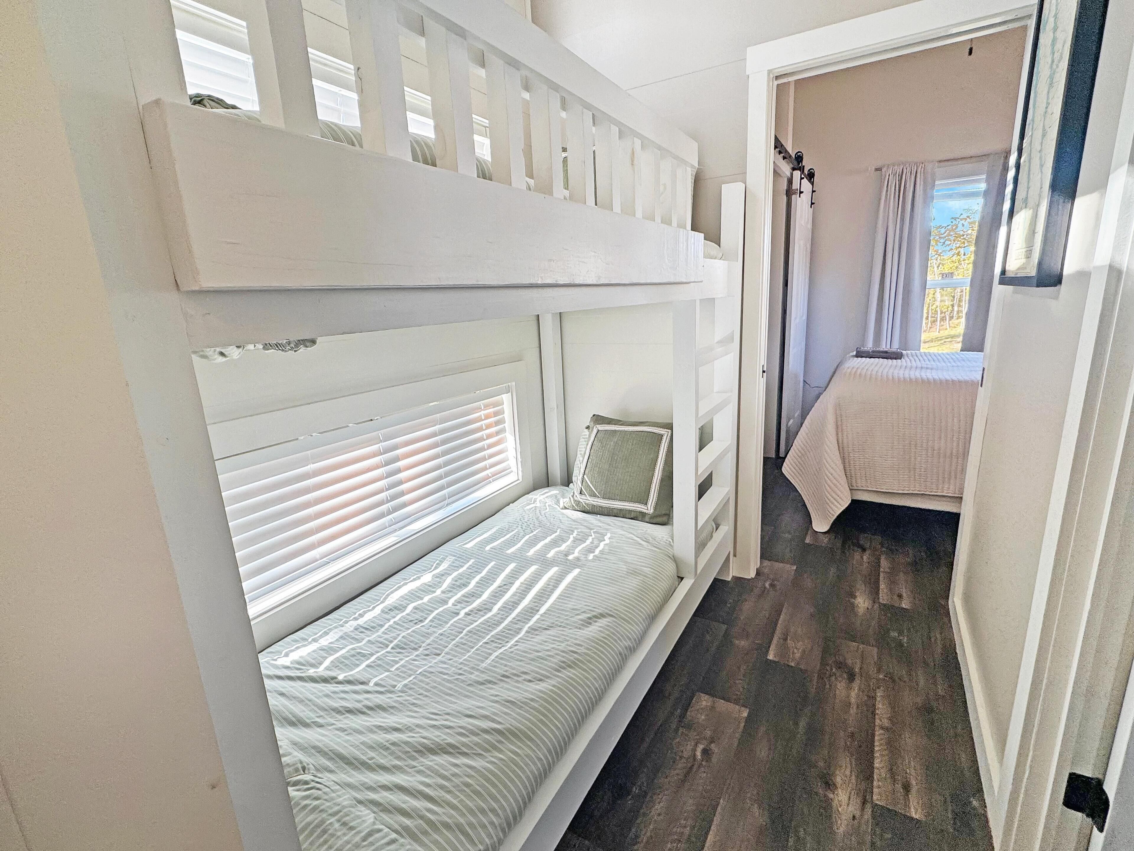 A bunk bed with a headboard, a bedside table, and a window with blinds.