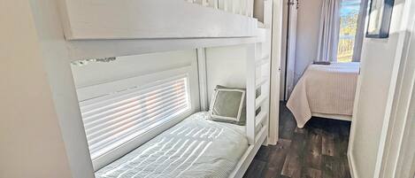 A bunk bed with a headboard, a bedside table, and a window with blinds.