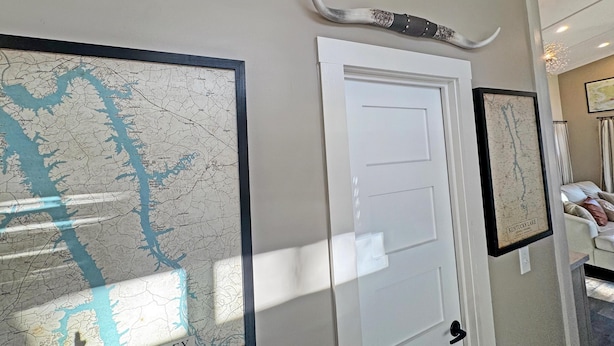 A hallway with a framed map of Barley, a white door, and a mounted horn. - Cottage Between the Lakes ("In The Pines" at KY Lake) | 105 Pine Grove Lane, Dover, TN 37058 (Dover)