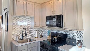 A kitchen with white cabinets, a black microwave, and a hexagonal tile backsplash. - Cottage Between the Lakes ("In The Pines" at KY Lake) | 105 Pine Grove Lane, Dover, TN 37058 (Dover)