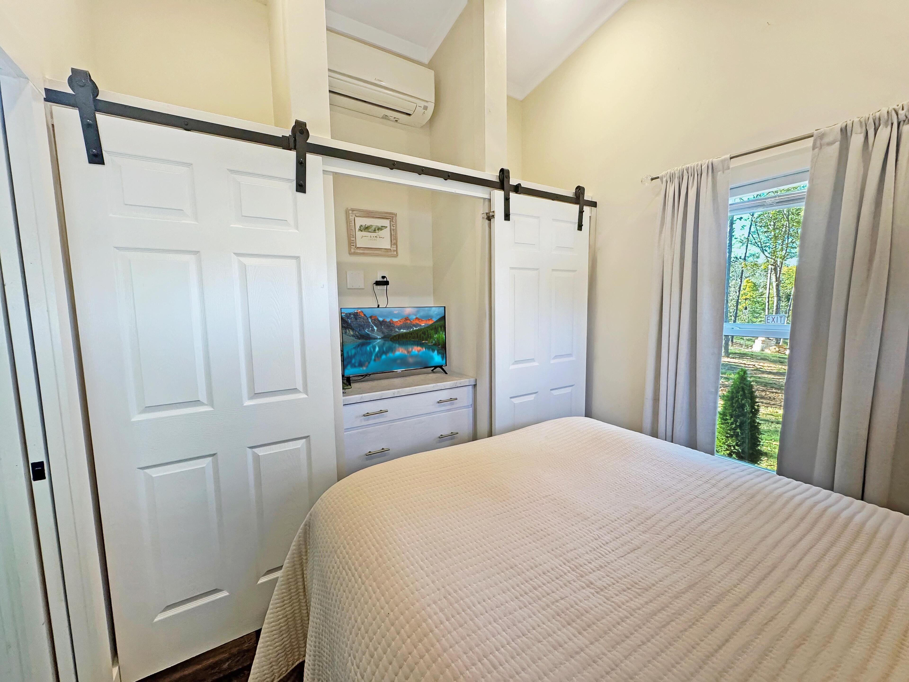 A bedroom with a bed, a wardrobe, a television, and a window with curtains.