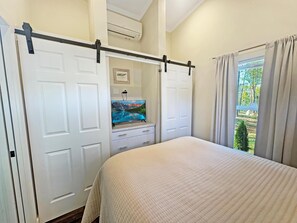 A bedroom with a bed, a wardrobe, a television, and a window with curtains. - Cottage Between the Lakes ("In The Pines" at KY Lake) | 105 Pine Grove Lane, Dover, TN 37058 (Dover)