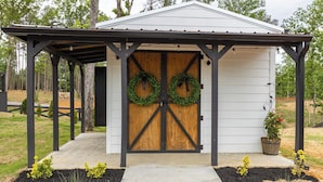 A small wooden shed with a metal roof and two wreaths on the door. - Cottage Between the Lakes ("In The Pines" at KY Lake) | 105 Pine Grove Lane, Dover, TN 37058 (Dover)