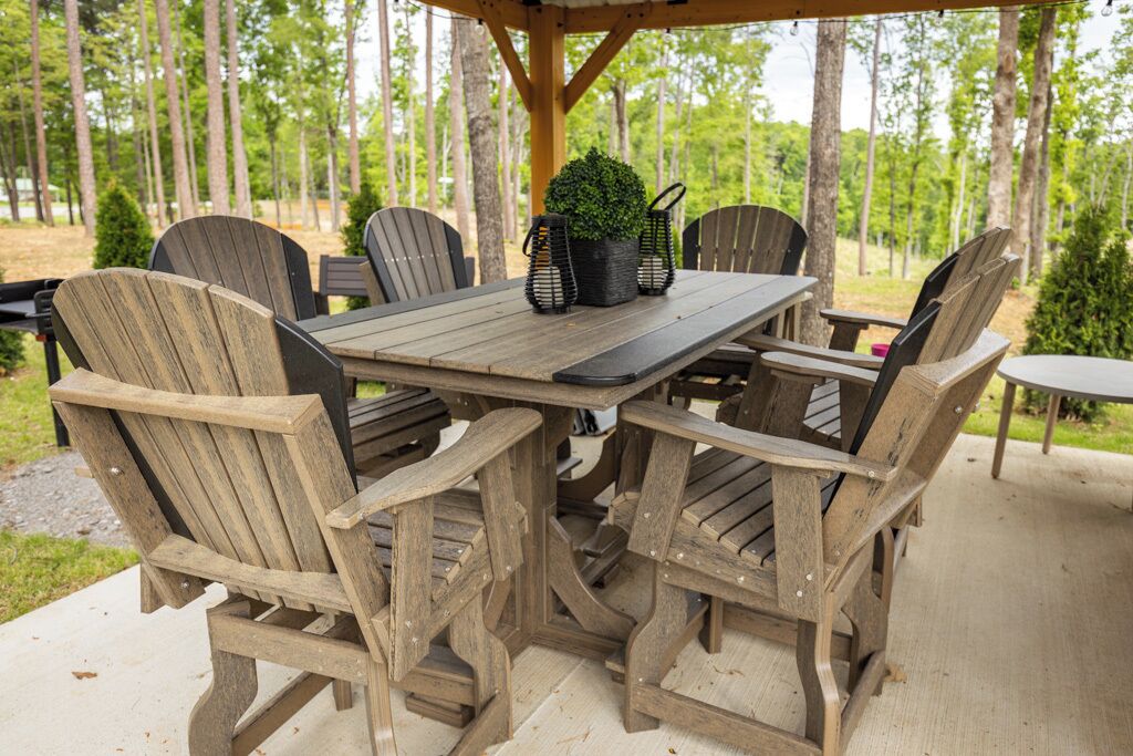 Un área de comedor al aire libre con madera, que incluye una mesa y sillas, rodeada de árboles.