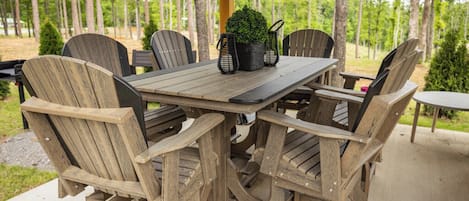 Un espace de repas extérieur en bois, avec une table et des chaises, entouré d’arbres.