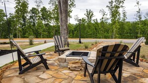 An outdoor seating area with Adirondack chairs and a stone fire pit. - Cottage Between the Lakes ("In The Pines" at KY Lake) | 105 Pine Grove Lane, Dover, TN 37058 (Dover)
