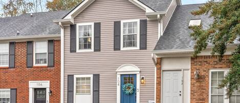 A two-story residential building with a front porch, a blue door, and a brick facade.