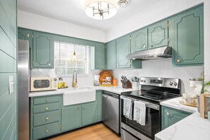 A kitchen with teal cabinets, a stainless steel refrigerator, a microwave, a dishwasher, a stove, and a window with blinds.