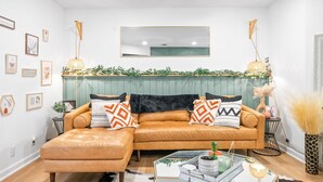 Ein Wohnzimmer mit einem braunen Ledersofa, einem Glastisch und einer grünen Wand mit einem Spiegel darüber.
