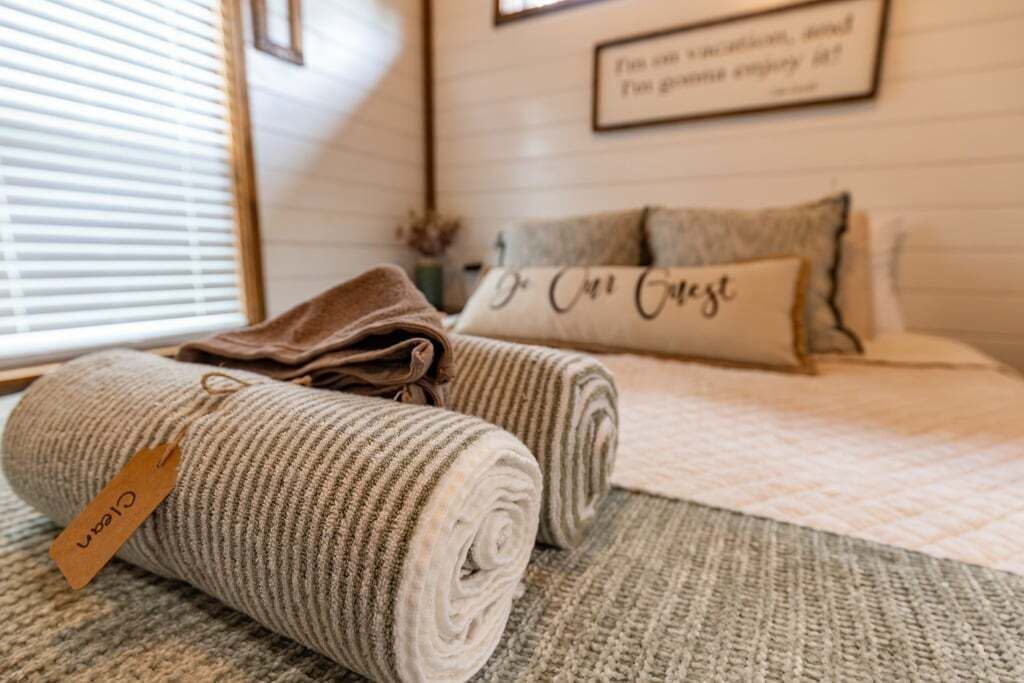 Een netjes opgemaakt bed met een gewatteerde dekbedovertrek en een kussen met de tekst 'Do it Guest'.