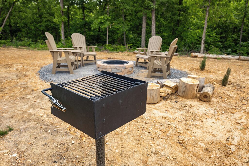 Ein Grill mit Feuerstelle, umgeben von Adirondack-Stühlen und einer natürlichen Umgebung.