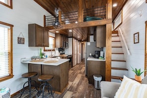 Une cuisine spacieuse avec des poutres en bois, un îlot central, des tabourets de bar et un escalier menant à un niveau supérieur.