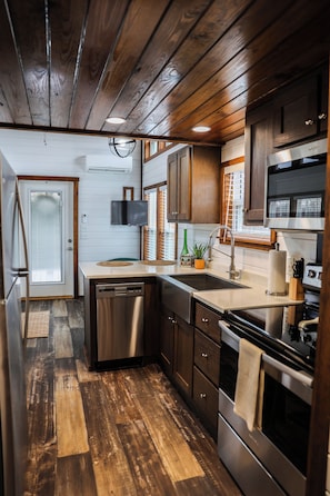 Una cocina compacta con suelo de madera, electrodomésticos de acero inoxidable y un horno empotrado.
