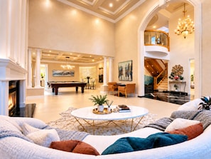 A spacious living room with a pool table, a fireplace, and a seating area with multiple couches.