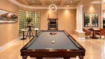 A pool table with a 'CPB Royal Apex' label, surrounded by a modern interior with a chandelier, artwork, and a fireplace.