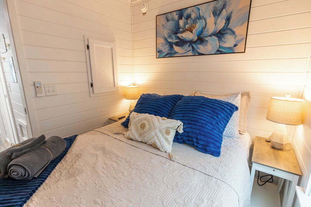A bedroom with a bed, two bedside lamps, a painting, and a rolled towel on the floor.