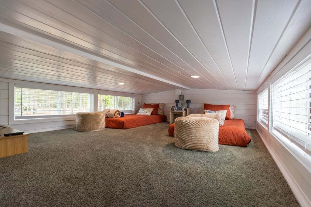 Een gezellige slaapkamer met een schuine kap, twee bedden met rode beddengoed, een klein houten nachtkastje en een groot raam.
