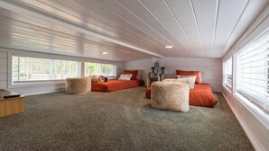 A cozy bedroom with a sloped ceiling, two beds with red bedding, a small wooden nightstand, and a large window.