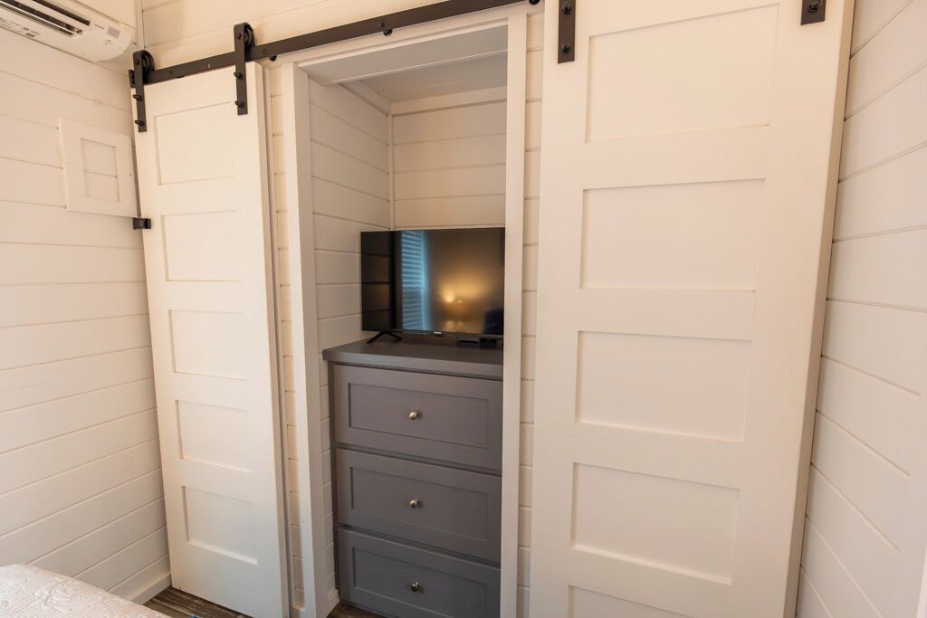 Una habitación con puerta corredera, un escritorio pequeño con cajones y un televisor sobre un mueble.