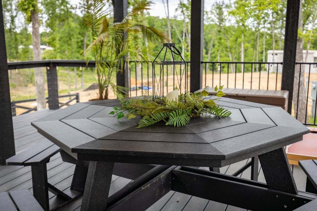 Een houten terras met een tafel en banken, omgeven door groen en een metalen hekwerk.