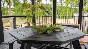 A wooden deck with a table and benches, surrounded by greenery and a metal railing.