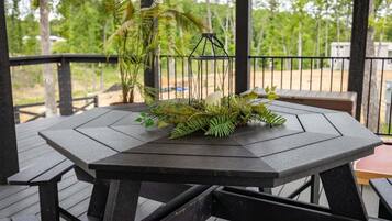 Een houten terras met een tafel en banken, omgeven door groen en een metalen hekwerk.