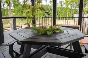 Een houten terras met een tafel en banken, omgeven door groen en een metalen hekwerk.